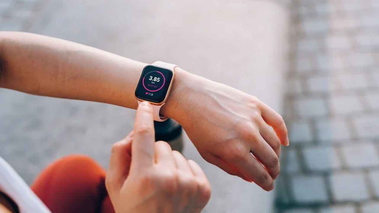 نمای بالای شانه از یک زن ورزشکار جوان آسیایی که پس از تمرین در فضای باز در شهر، آمار تناسب اندام خود را روی ساعت هوشمند بررسی می‌کند تا پیشرفت تمرین خود را نظارت کند.